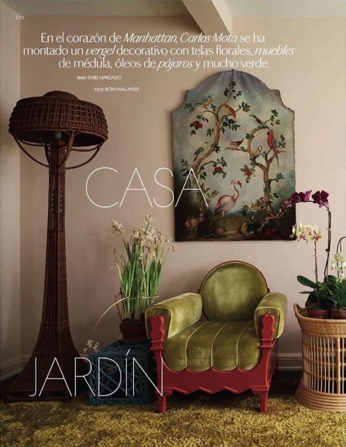 Living room interior featuring a green velvet chair, a wicker floor lamp, white flowers, and a framed painting with bird motifs.