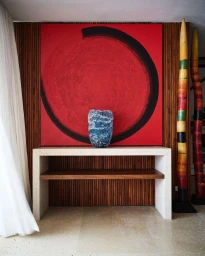 Blue textured vase sitting on a white console table in front of a large red abstract painting with a black circular brushstroke.
