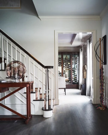 Interior view of an elegant home hallway featuring a wooden staircase, console table with glass lamp, and open doorway into a dining area
