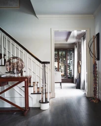 Interior view of an elegant home hallway featuring a wooden staircase, console table with glass lamp, and open doorway into a dining area