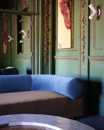 Blue velvet sofa against green paneled walls with gold molding and modern white wall sconces photographed by Bjorn Wallander
