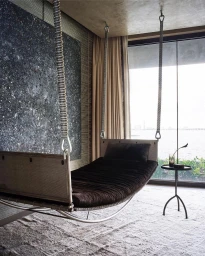 Suspended hanging daybed in a modern luxury interior with textured walls and a large window overlooking the water.