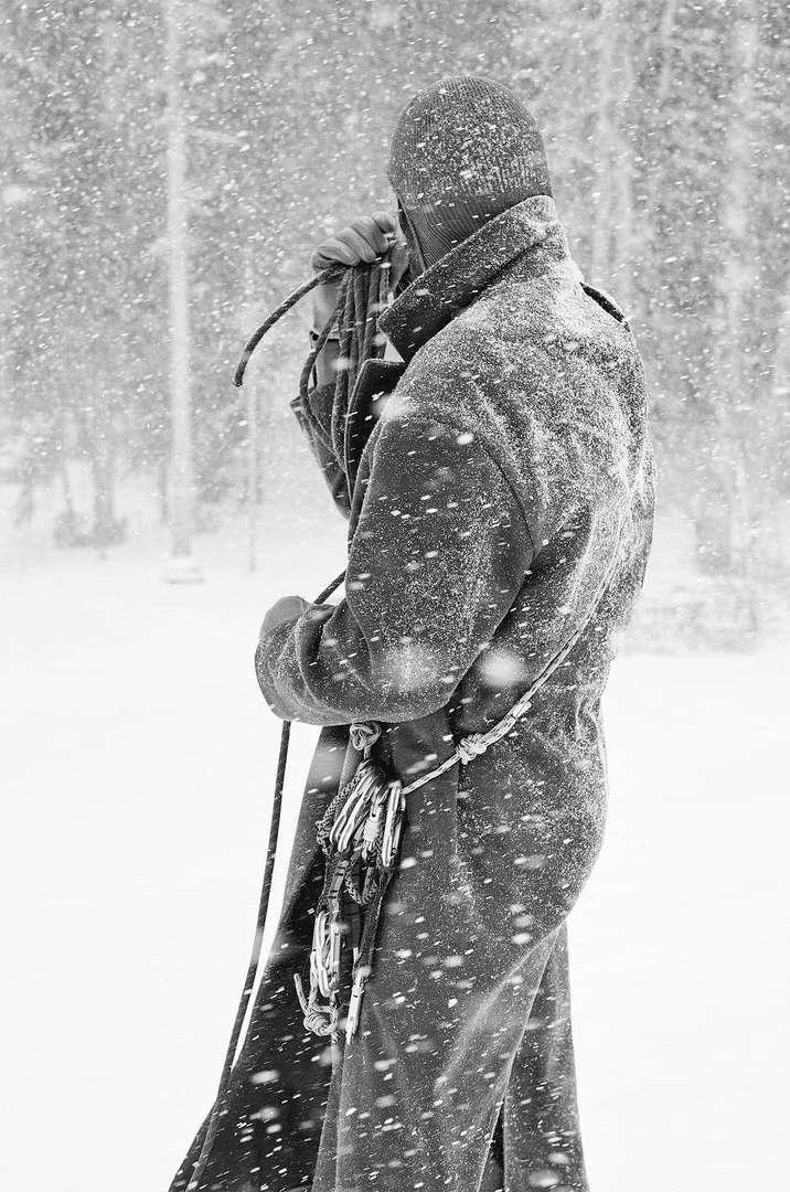 Person in winter coat with snow and climbing rope outdoors. Back view of outdoor apparel and gear in a snowy, forest environment.