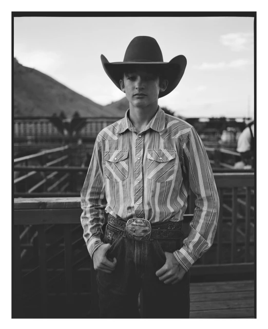 Black-and-white portrait of a teenage boy in a cowboy hat and western shirt, standing in front of a mountain landscape.