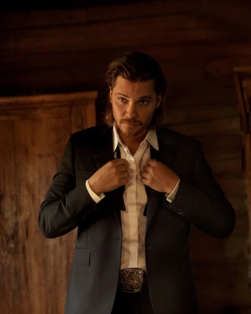 Man in black suit adjusts tie in rustic setting, showcasing modern Western fashion with a hint of old-world charm and rich wooden textures.