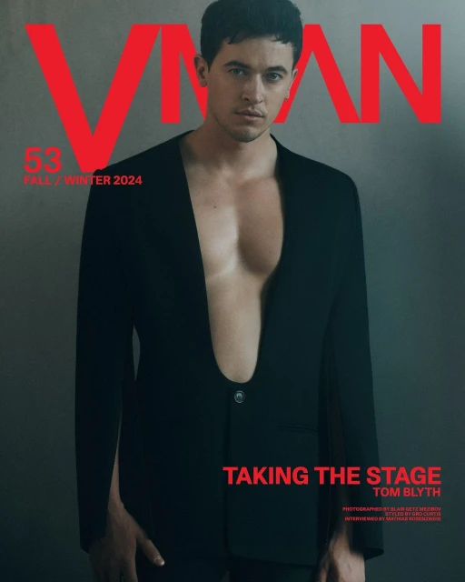 Tom Blyth on VMAN magazine cover, Fall/Winter 2024. Man in black suit, open chest, red masthead. Fashion editorial portrait, studio shot.