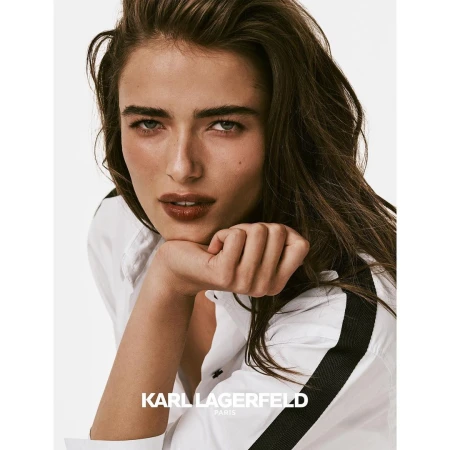 Close-up portrait of a woman resting her chin on her hand wearing a white shirt with black shoulder stripes.