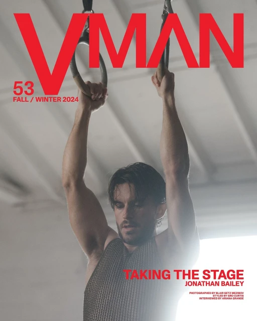 VMAN magazine cover featuring adult male holding gymnastic rings, photographed indoors with bright lighting and large red magazine title.