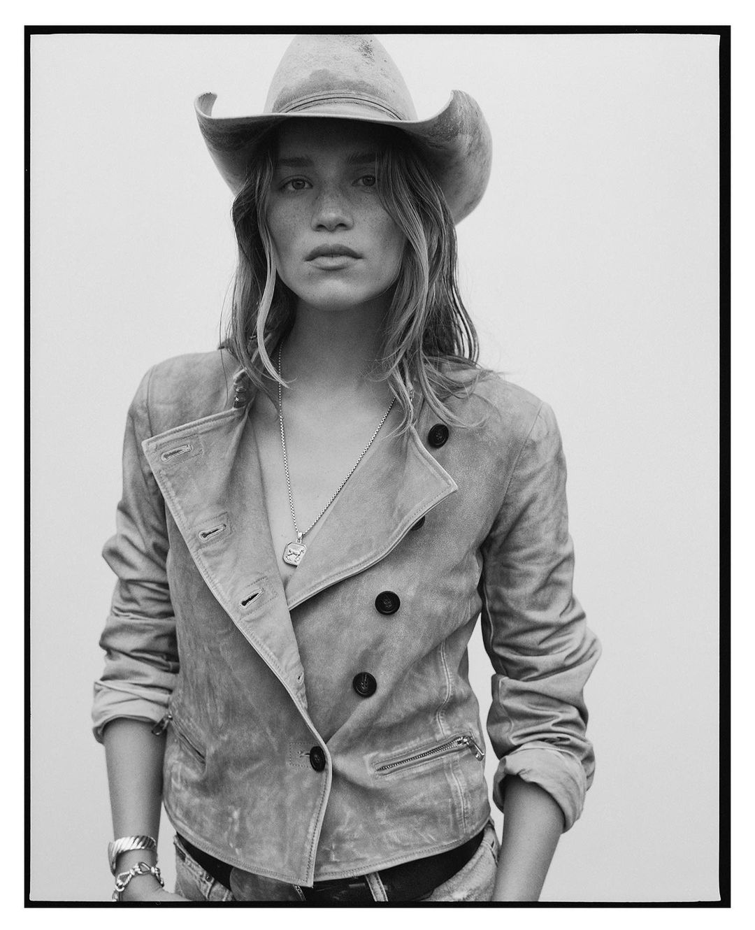 Monochrome portrait of a woman wearing a cowboy hat and a double-breasted jacket, looking directly at the camera, against a plain backdrop.