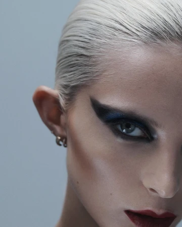 Close-up portrait of a woman with slicked-back blonde hair, dark winged eye makeup, and dark red lipstick, photographed by Blair Getz Mezibov.