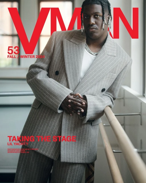 Lil Yachty poses on a fashion magazine cover wearing a grey pinstripe suit with red and black text overlay in an indoor setting.