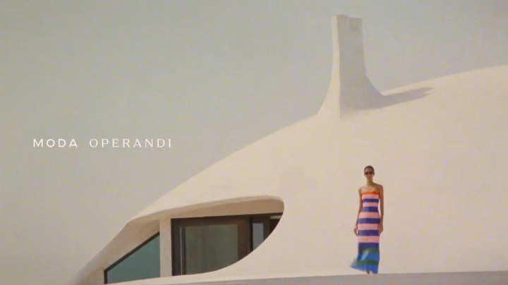 Fashion shot of a woman in a striped dress, standing in front of a white, modern architectural building, sunglasses, outdoors.
