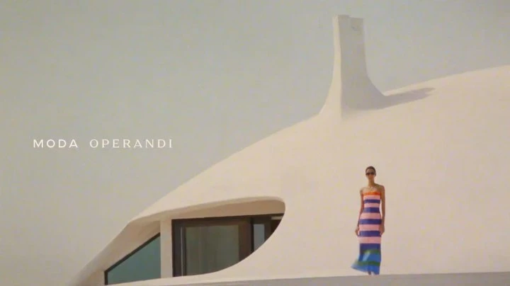 Fashion shot of a woman in a striped dress, standing in front of a white, modern architectural building, sunglasses, outdoors.