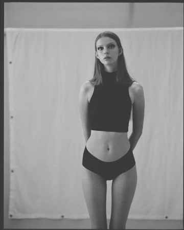 Portrait of a female model in black two piece outfit standing against a white backdrop.