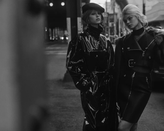 Two women posing on a city street in black glossy coats and leather outfits captured in monochrome by Blair Getz Mezibov.