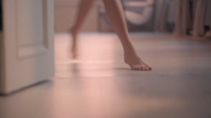 Bare feet walk across a light floor, with a white door slightly ajar on the left, creating a minimalistic, serene indoor scene.