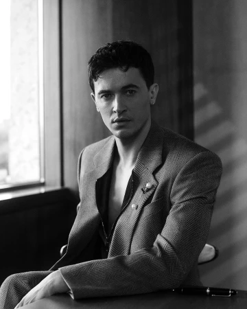 Portrait of a man in a patterned blazer seated at a table indoors by a window, captured in monochrome by Blair Getz Mezibov.