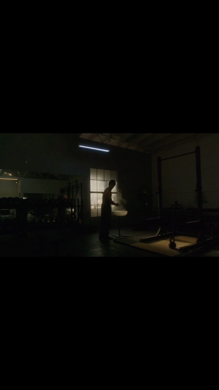 Silhouette of an adult male working out in a dark indoor gym space with weights and exercise equipment. Fitness, sports, exercise.