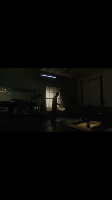 Silhouette of an adult male working out in a dark indoor gym space with weights and exercise equipment. Fitness, sports, exercise.