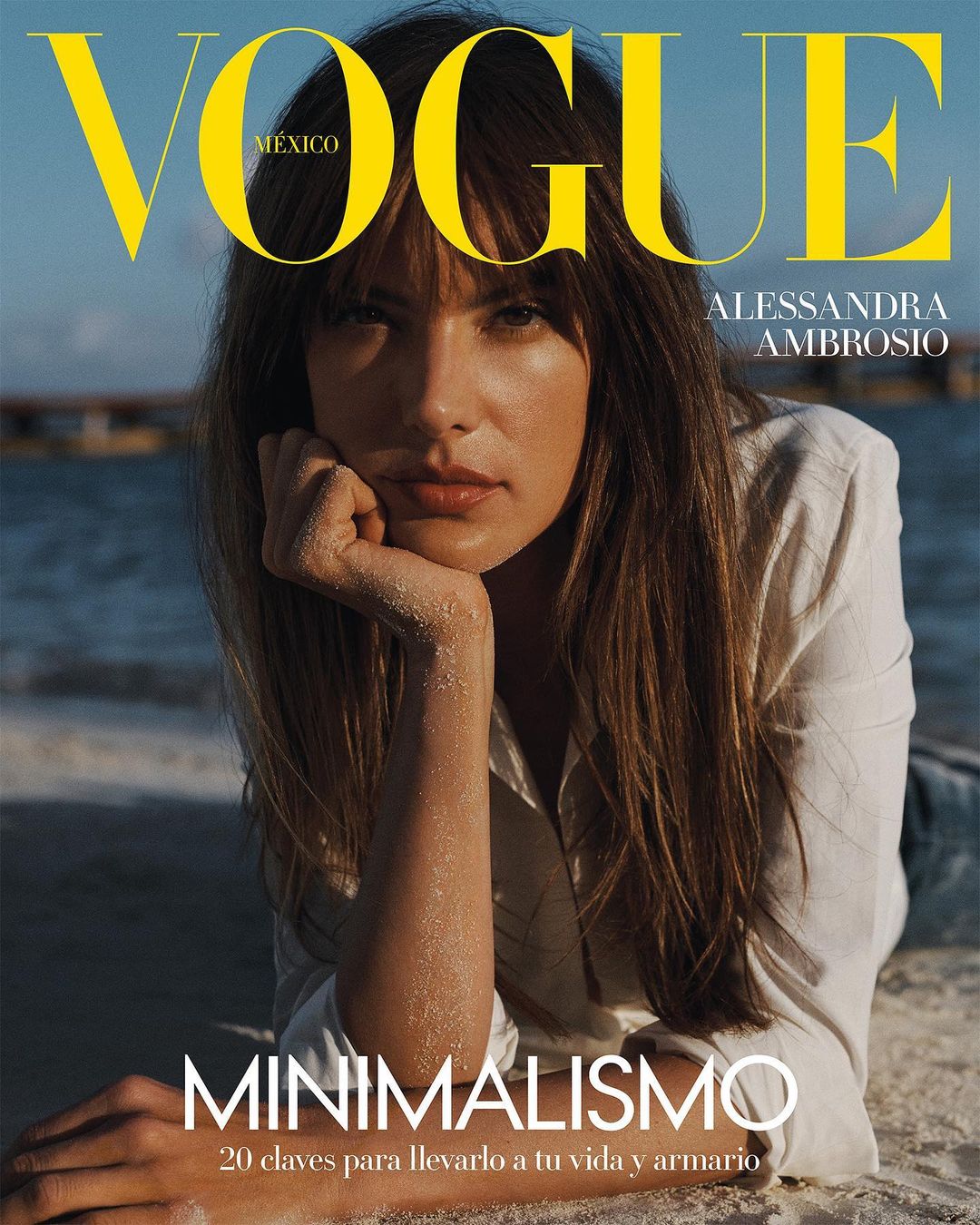Alessandra Ambrosio on Vogue Mexico cover, laying on the beach. She is wearing a white shirt and looking at the camera.
