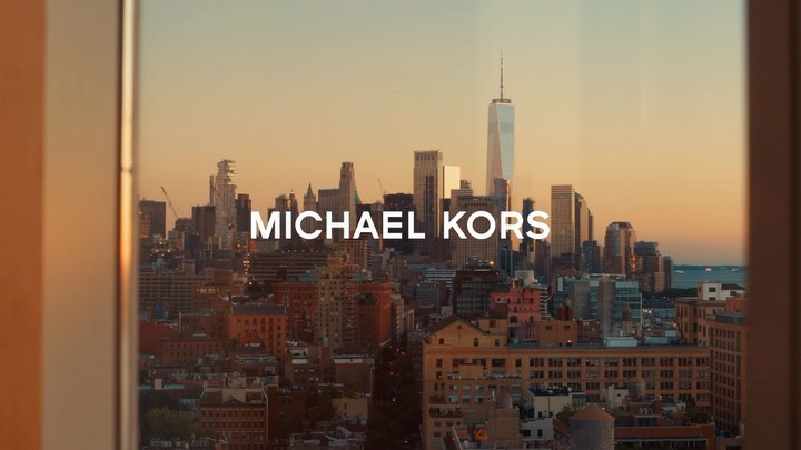 New York City skyline featuring skyscrapers and a cityscape seen through a window with the text MICHAEL KORS overlaid.