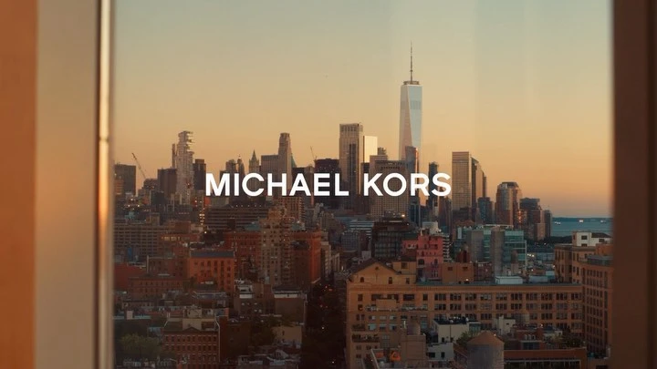 New York City skyline featuring skyscrapers and a cityscape seen through a window with the text MICHAEL KORS overlaid.