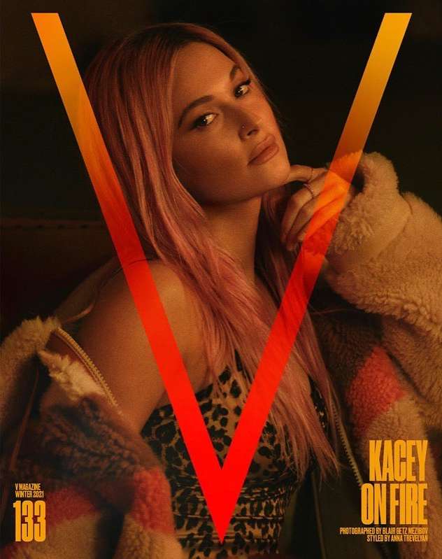 Magazine cover featuring Kacey Musgraves with pink hair, wearing animal print, a sherpa coat, and the letter V in orange overlaid.