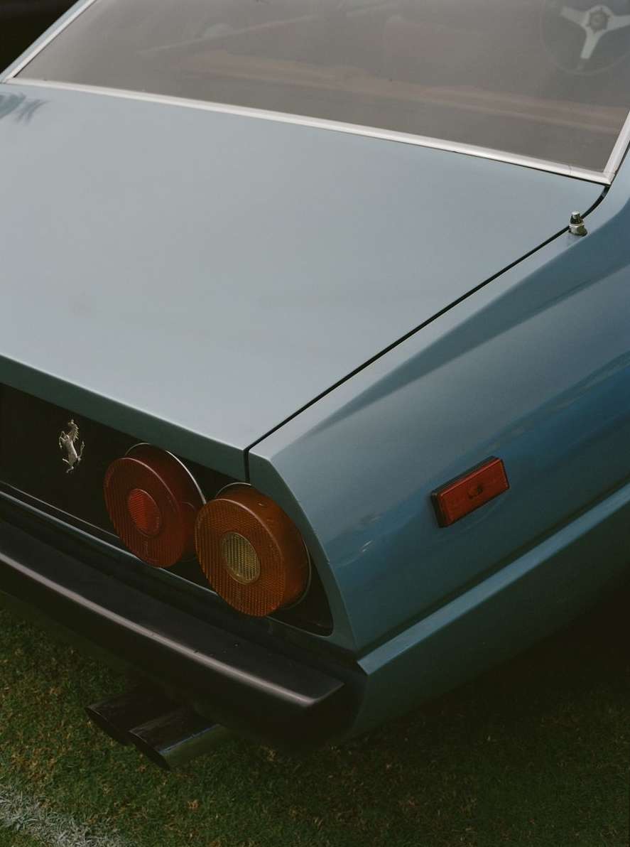Close-up of a classic light blue Ferrari, featuring its rounded taillights, black bumper, and the iconic Ferrari emblem on the rear panel.