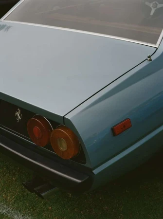 Close-up of a classic light blue Ferrari, featuring its rounded taillights, black bumper, and the iconic Ferrari emblem on the rear panel.