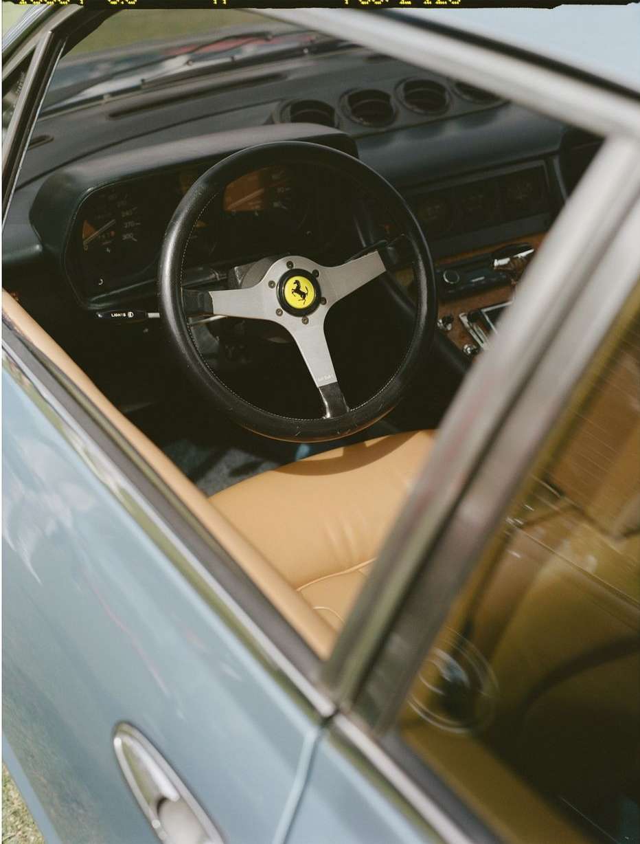 Ferrari interior view through open driver's side window, focusing on the steering wheel and dashboard, showcasing car's vintage design.