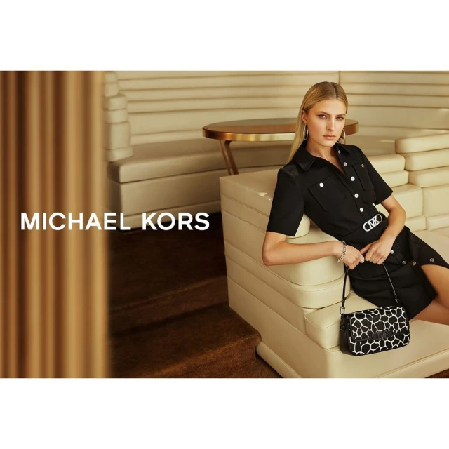 A woman in a black dress sitting on a couch next to a purse. The image also contains the words, MICHAEL KORS.