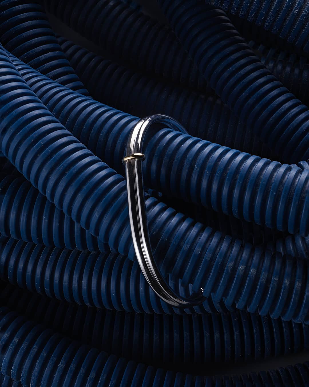 Close-up of a blue corrugated flexible conduit with a metal hook, showcasing its texture, design, and industrial application.