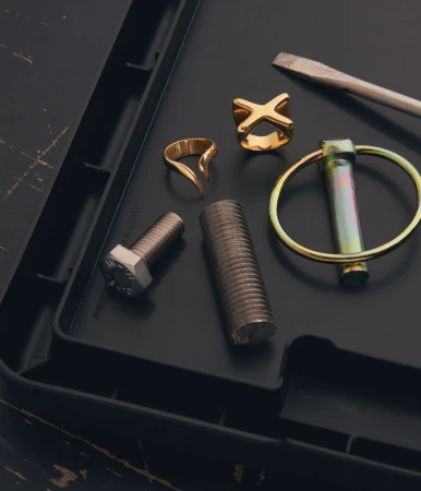Still life of mechanical parts: bolts, ring, and screwdriver arranged on a textured black surface in a studio setting.