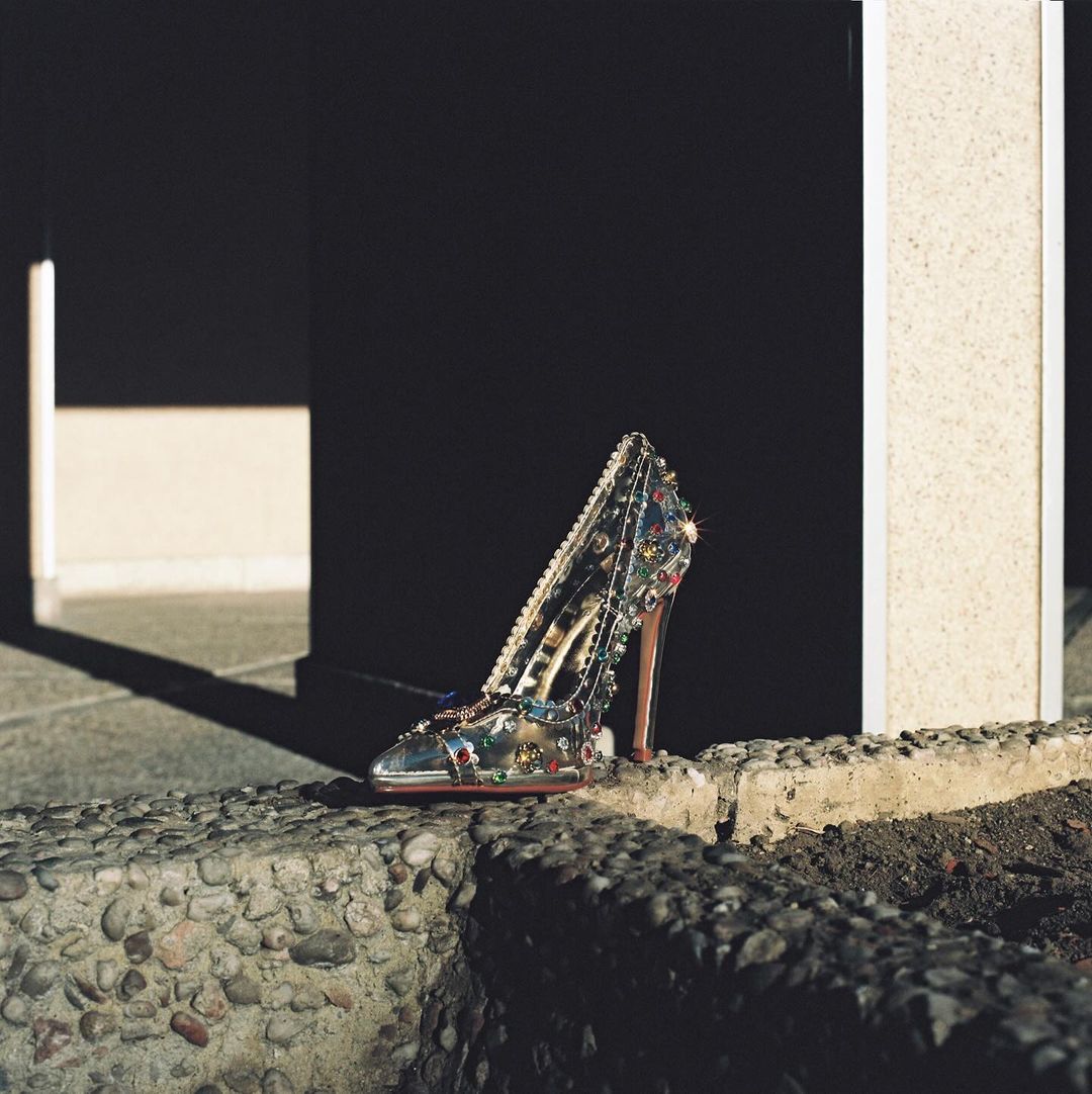 Glamorous high-heeled shoe adorned with jewels placed on a concrete ledge against a modern architectural background, reflecting luxury and fashion.