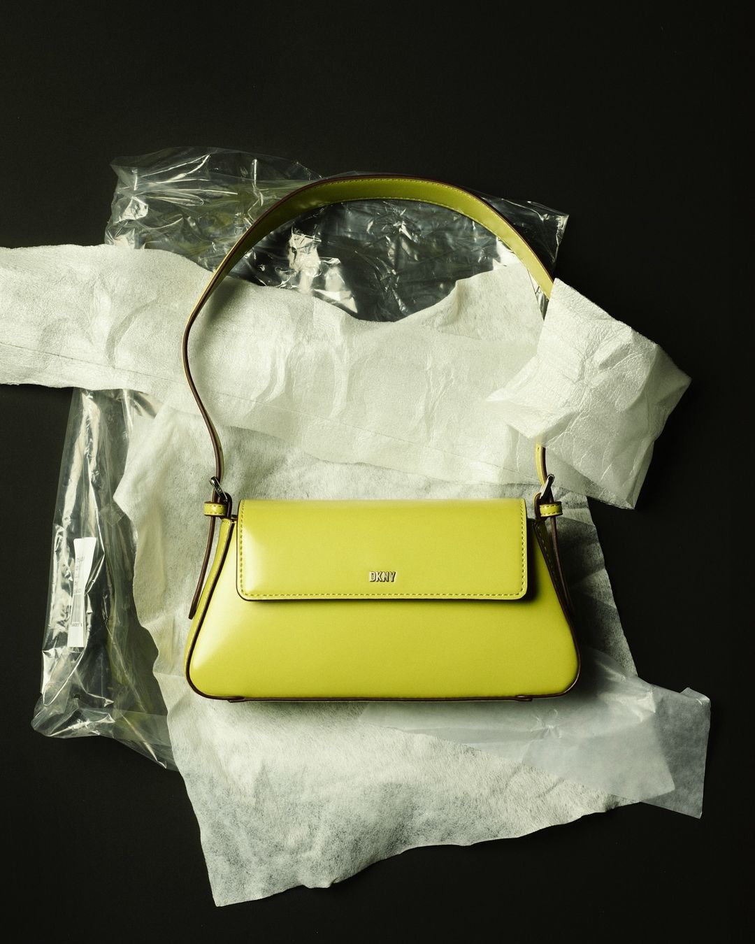 A bright-yellow purse on wrinkled white and clear plastic, against a dark background, creates a striking contrast in fashion photography.