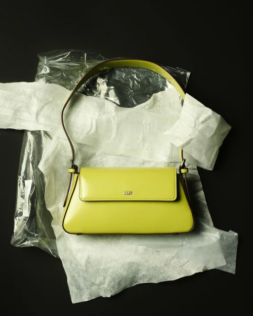 A bright-yellow purse on wrinkled white and clear plastic, against a dark background, creates a striking contrast in fashion photography.