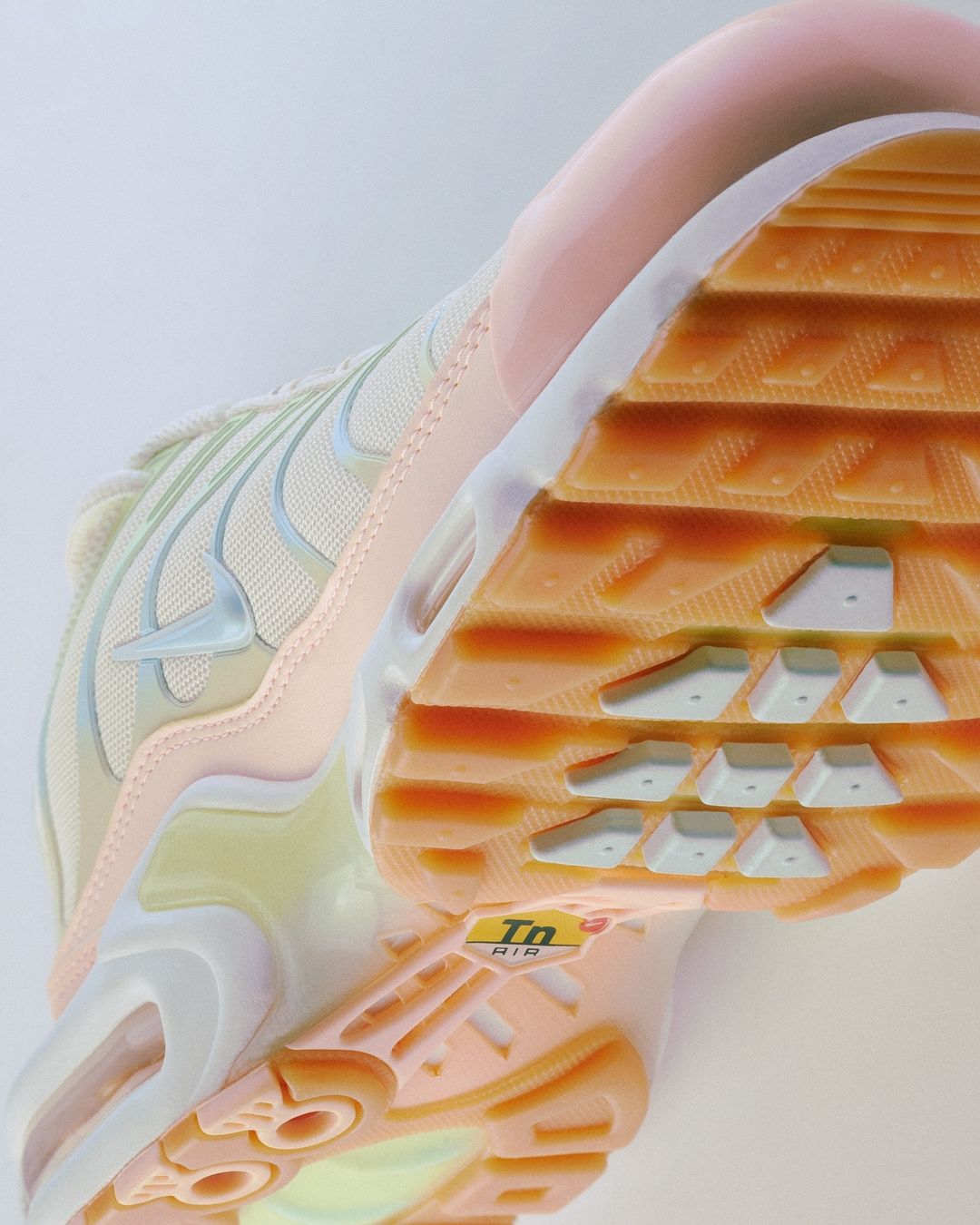 Close-up view of a peach and beige Nike Air Max Plus sneaker, highlighting its design and sole on a neutral background.
