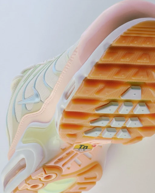 Close-up view of a peach and beige Nike Air Max Plus sneaker, highlighting its design and sole on a neutral background.