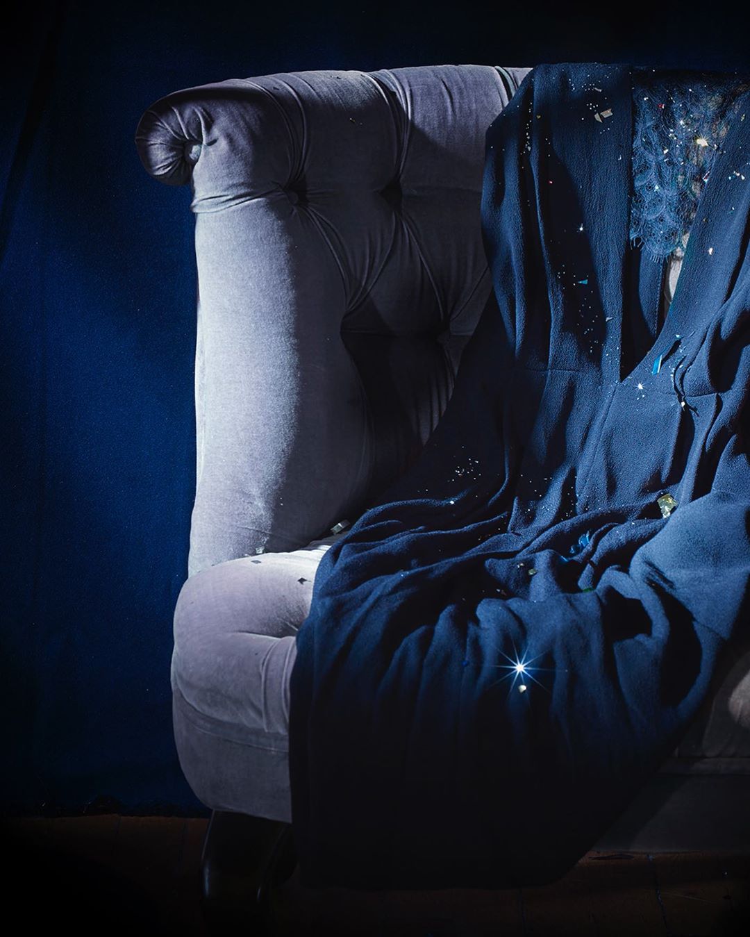 Elegant blue velvet armchair with a dark blue throw, softly illuminated against a dark background, highlighting textures and subtle details.