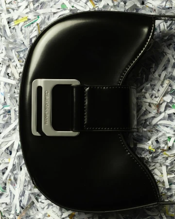 Black Calvin Klein Jeans handbag with silver buckle on a white shredded paper background in a studio product shot.