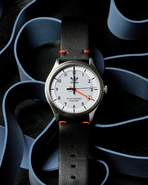Silver Adidas watch with a white face, black leather strap, and orange details against a dark background with light blue accents.