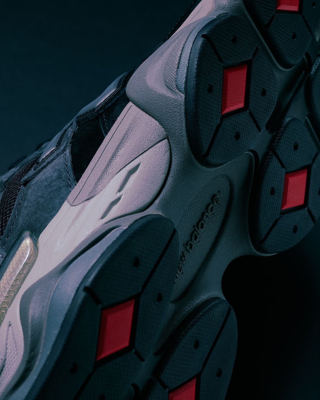 Close-up of a grey and black New Balance sneaker sole with red accents, showcasing its texture and design against a dark background.