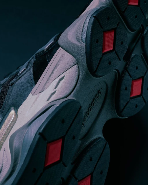 Close-up of a grey and black New Balance sneaker sole with red accents, showcasing its texture and design against a dark background.