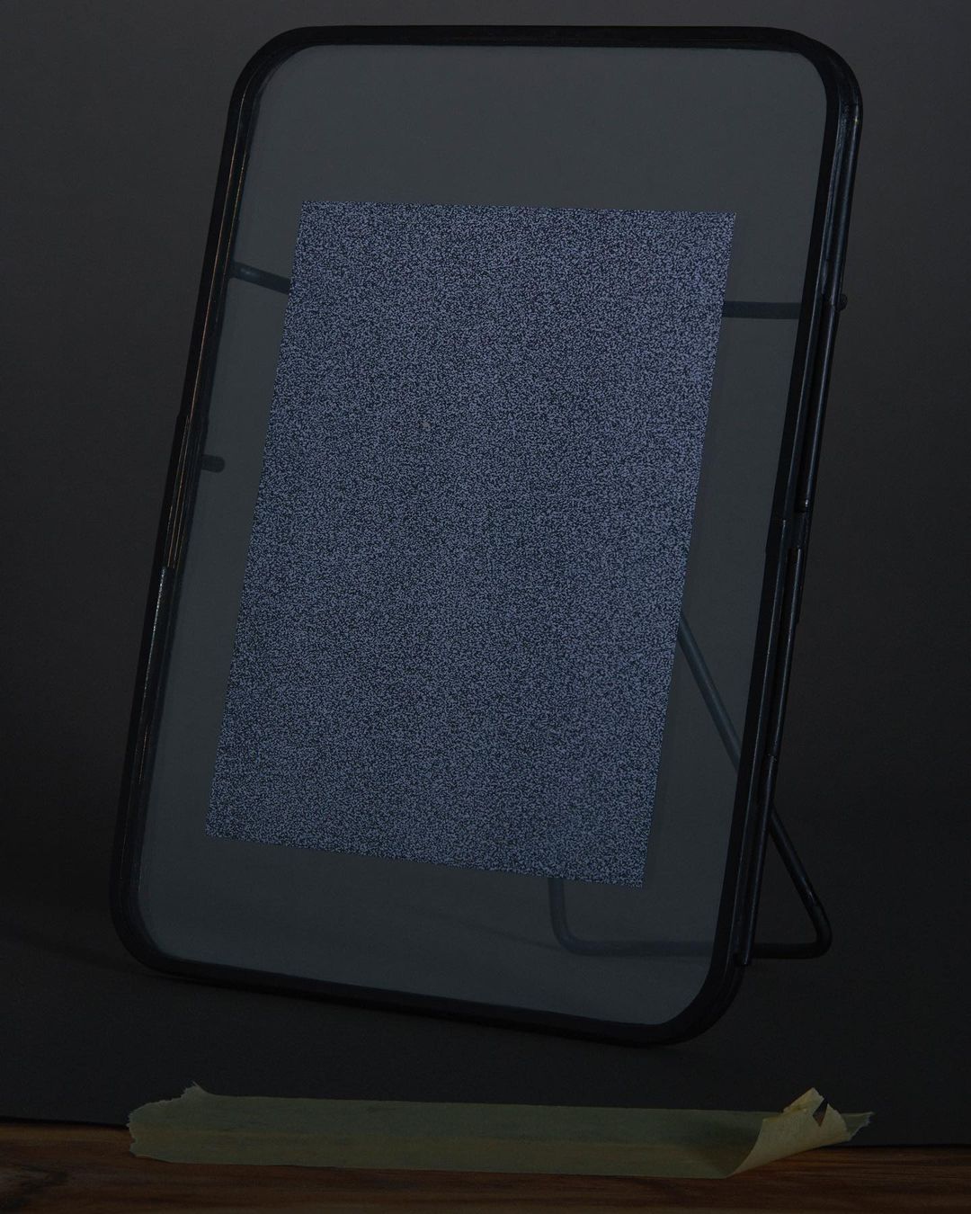 Framed paper with subtle speckled texture, presented on a dark background with a wooden base and supported by a stand, lit from above.