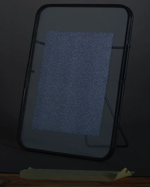 Framed paper with subtle speckled texture, presented on a dark background with a wooden base and supported by a stand, lit from above.