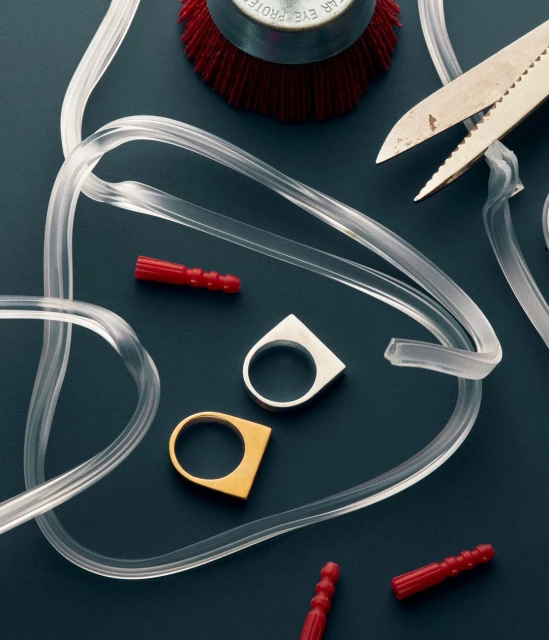 Jewelry making still life: two rings (gold and silver) are centered among clear tubing, red plugs, a brush head and metal snips.
