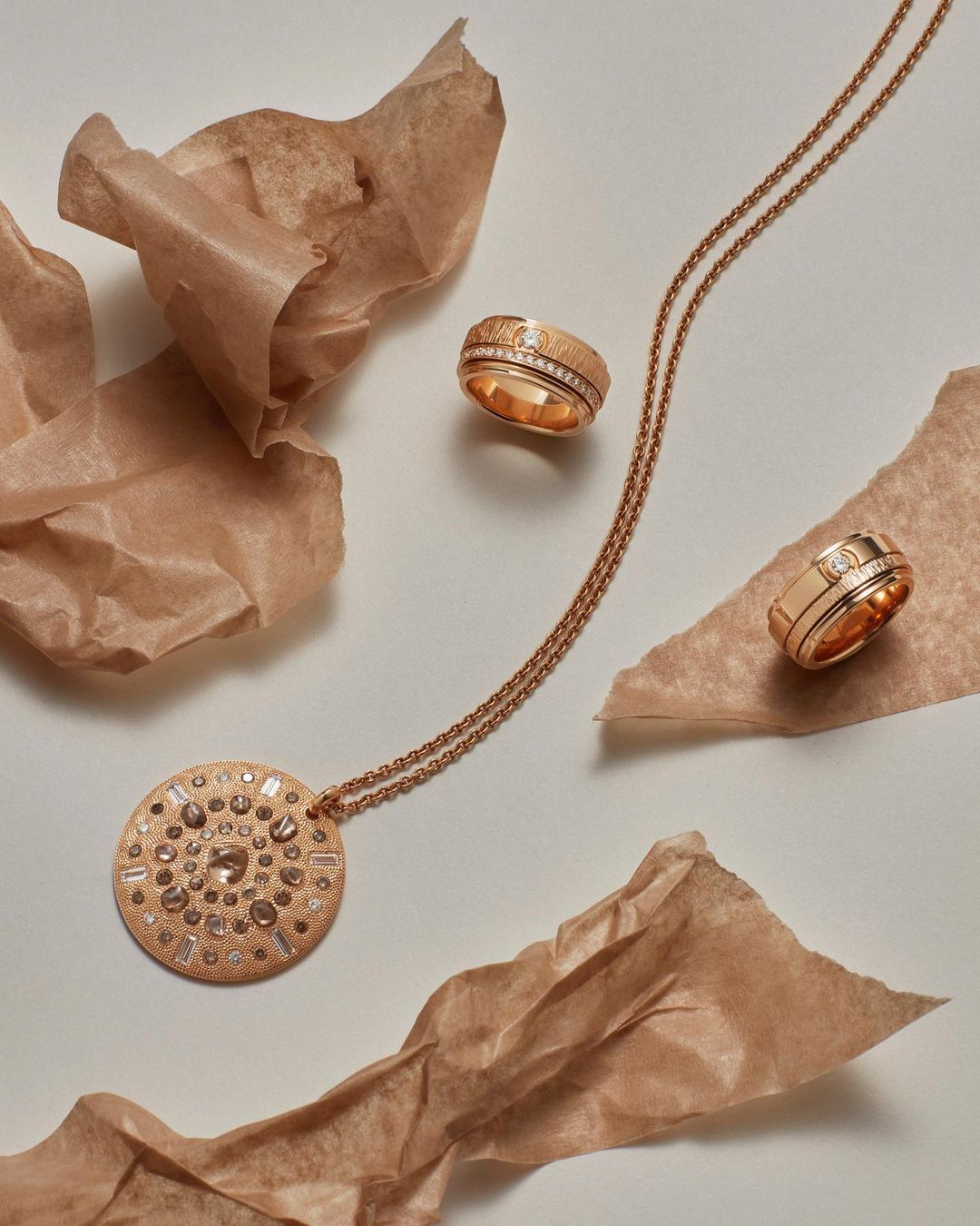 High-angle shot of rose gold necklace and rings on a white surface with crumpled brown paper, showcasing jewelry and studio lighting.