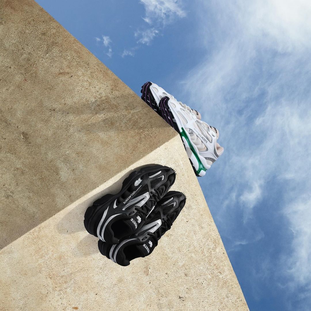 Elevated view of black and white running shoes on a concrete ledge against a partly cloudy sky. Athletic footwear product shot.