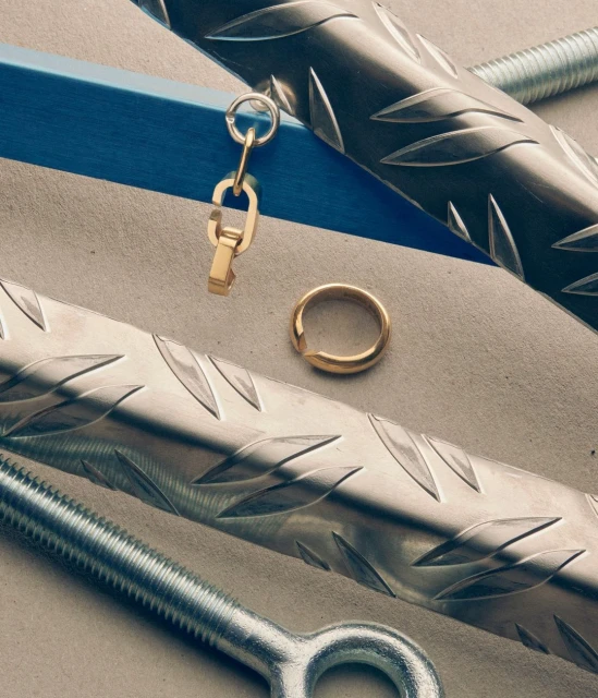 Studio shot of gold ring and keychain with metal rods and fasteners, showcasing jewelry and industrial design.