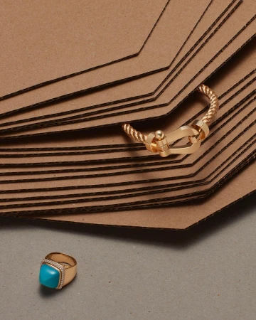 Close-up of a gold ring with a turquoise stone set on a gray surface with a stack of folded brown cardboard bags.